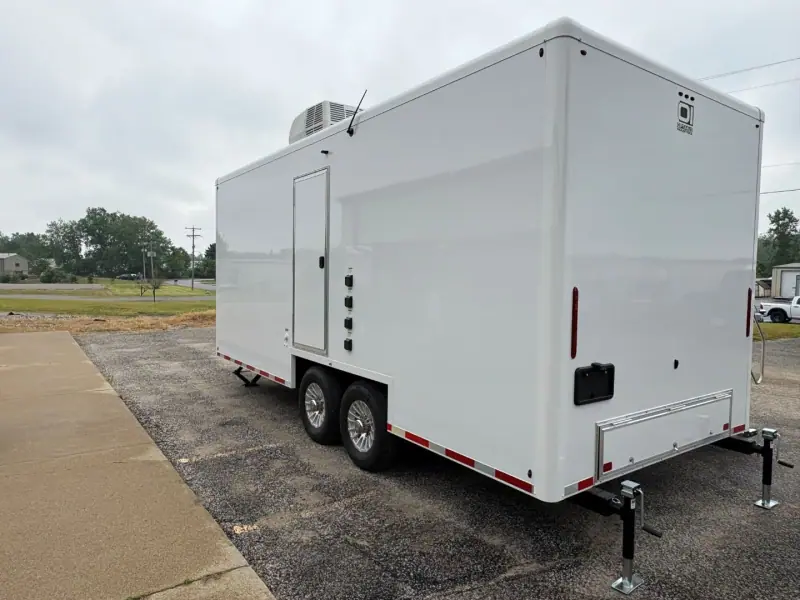 Tandem-axle restroom trailer seen from the front corner on a gravel lot
