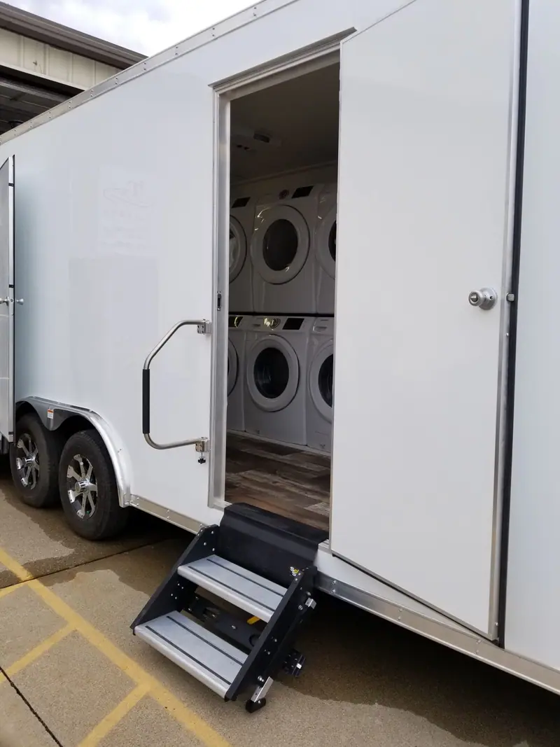 Laundry trailer with its door open on stacked washers and dryers and a fold-down step
