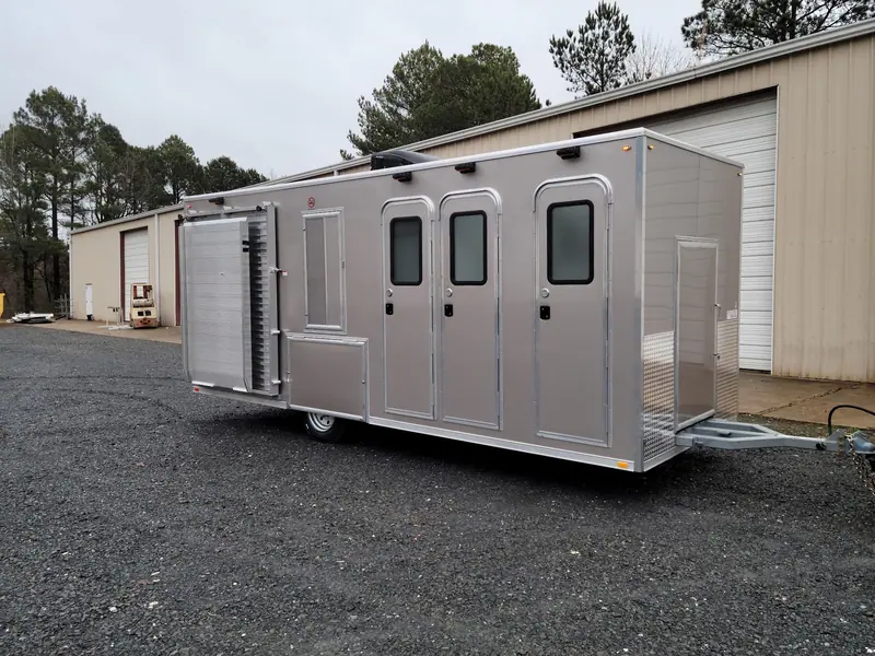 Long shower trailer with six private doors, parked on gravel outside the shop