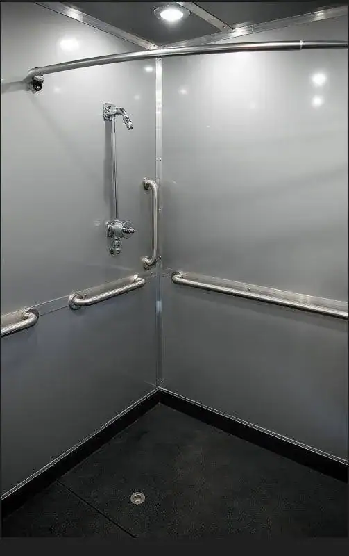 The ADA Single Restroom and Restroom Shower Trailer features a gray accessible shower with grab bars on two walls, a mounted showerhead, handheld shower, and a non-slip floor with central drain.