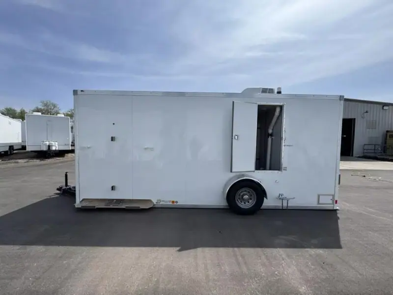 A large white enclosed trailer with one door open, parked on an asphalt surface outside an industrial building.