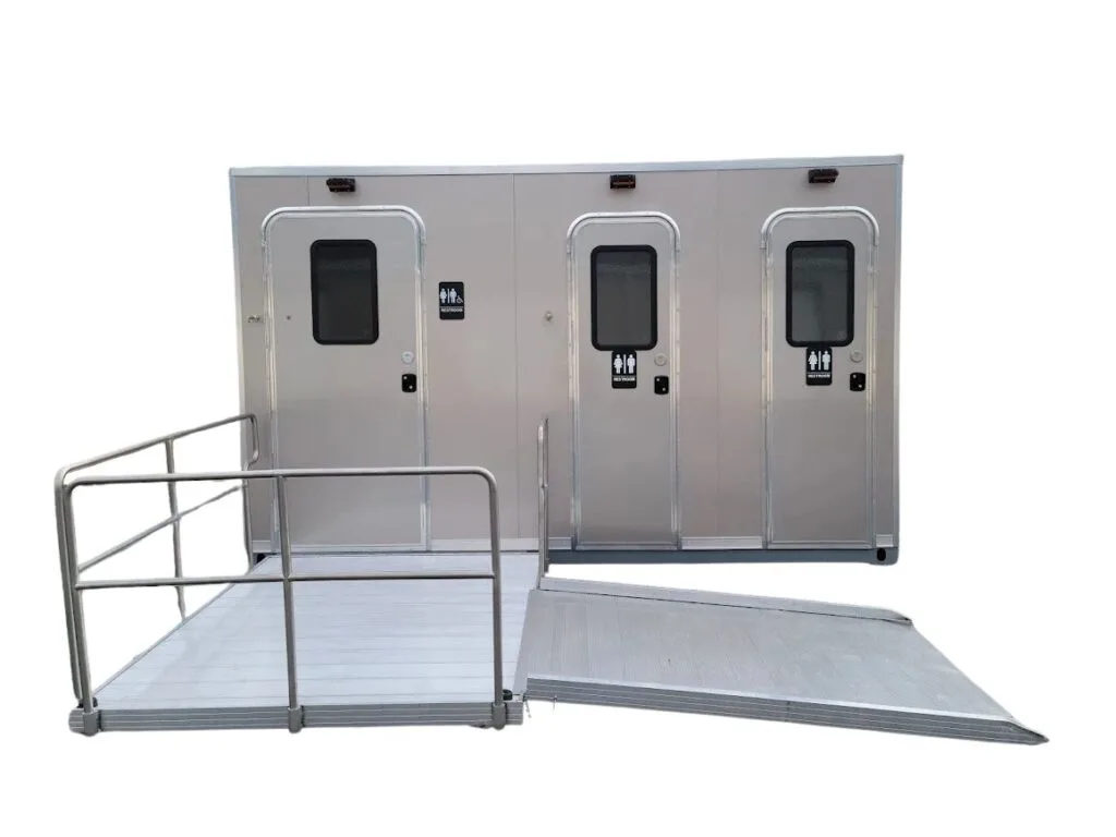 The CI 13 - 4 Stall ADA Restroom Skid (13 ft) is a silver portable restroom trailer with four stalls, featuring male and female signs plus front accessibility ramps.