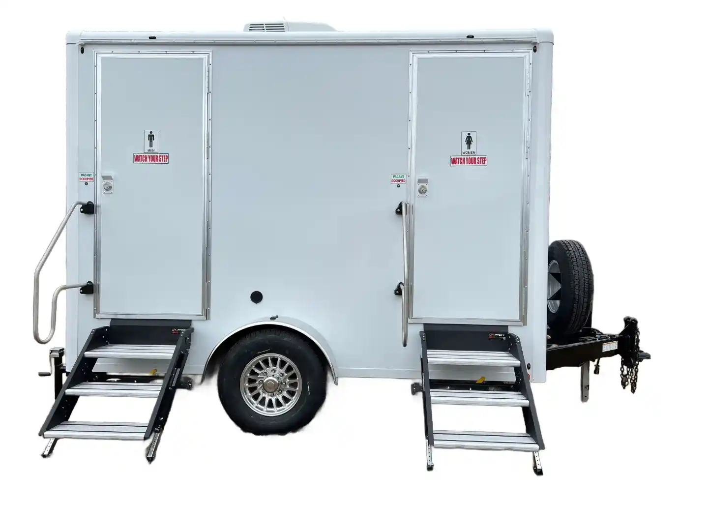 A white portable restroom trailer with two doors, each accessible by metal steps, and a spare tire mounted on the right side.