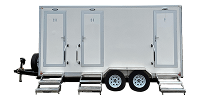 A white shower restroom trailer with three doors, each with a step leading up, mounted on a double-axle trailer.